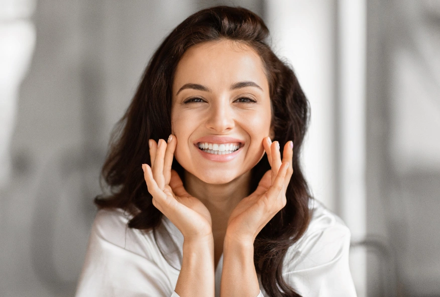 Smiling woman with hands near face in dental office setting, representing patient satisfaction and dental care.