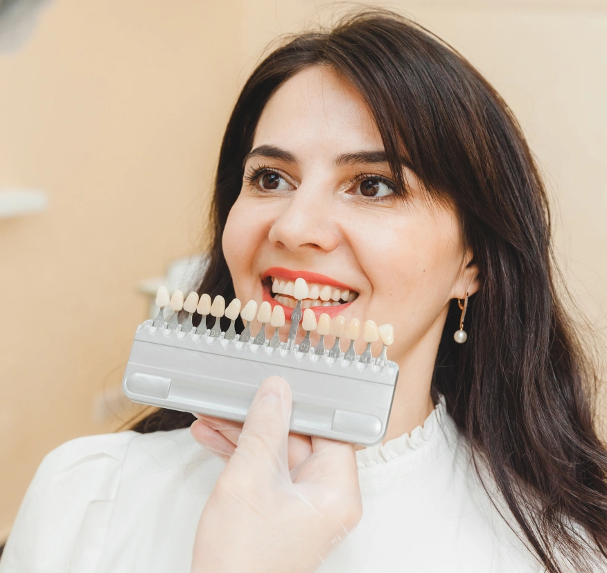 Woman comparing tooth shade samples to her natural teeth in dental office setting.