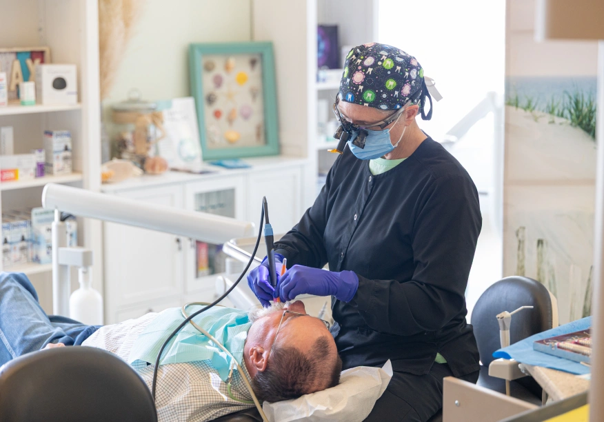 Dentist examines patient's teeth using intraoral camera in modern dental office treatment room.
