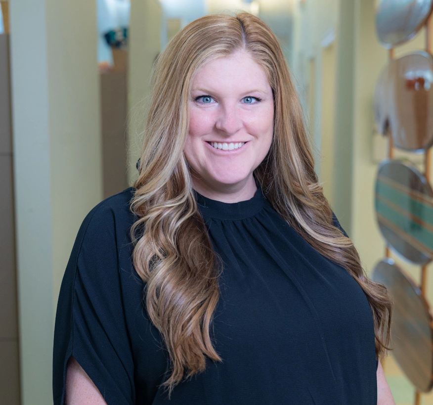 Professional woman smiling at camera in dental office hallway wearing black shirt.