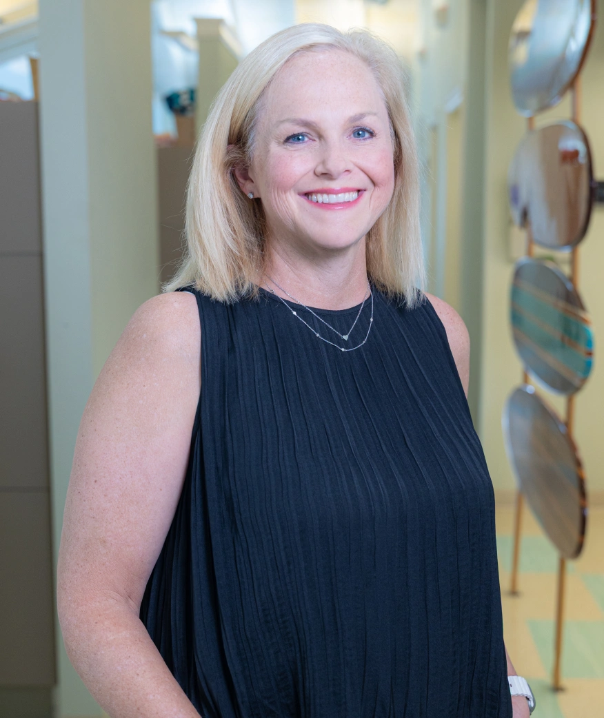 Professional woman smiling at camera in modern dental office hallway wearing black sleeveless top.