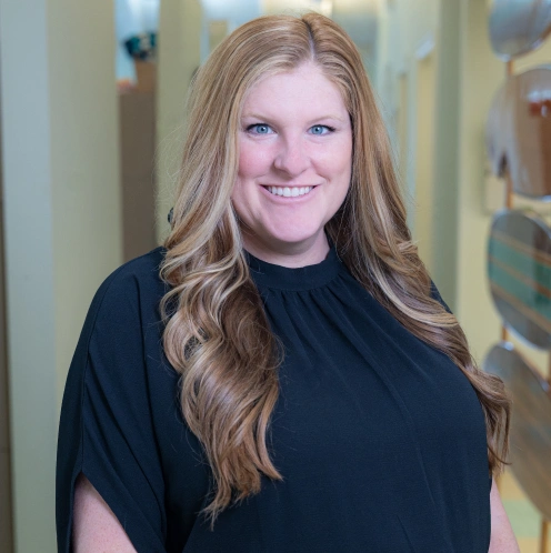 Professional woman smiling at camera in dental office hallway wearing black shirt.