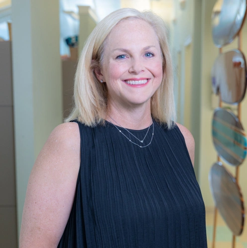 Professional woman smiling in dental office hallway, wearing black sleeveless top.